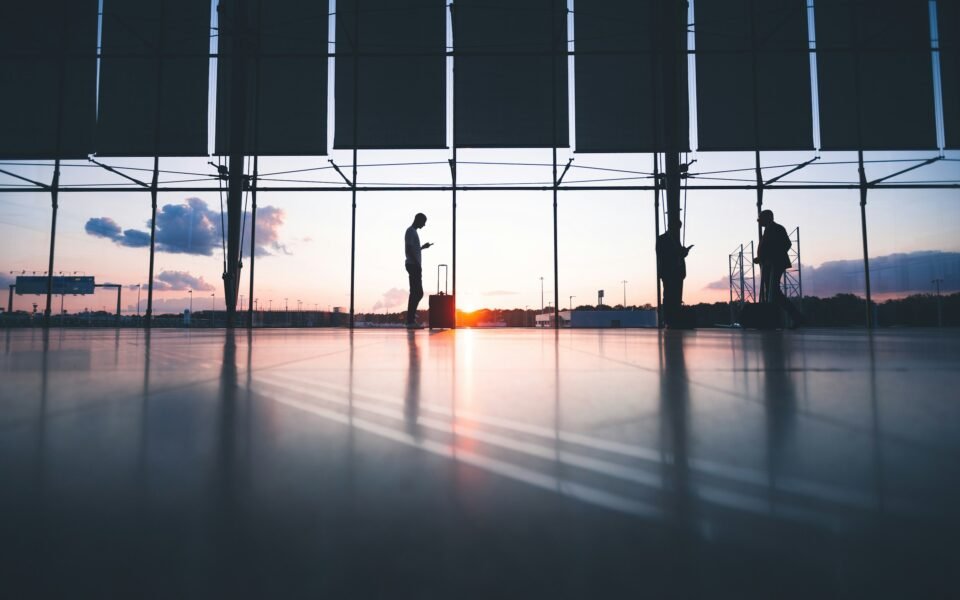 Siluetas de viajeros con maletas ante la cristalera de una terminal al atardecer