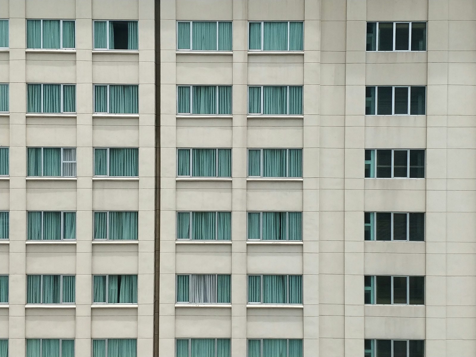Fachada de un edificio de hotel con filas de ventanas y cortinas verdes
