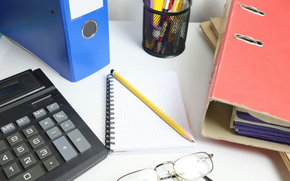 Calculadora, archivadores y cuaderno cuadriculado sobre una mesa de oficina