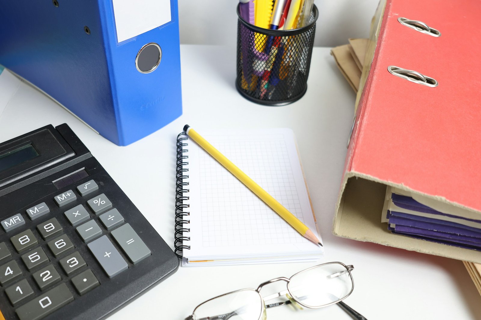 Calculadora, archivadores y cuaderno cuadriculado sobre una mesa de oficina