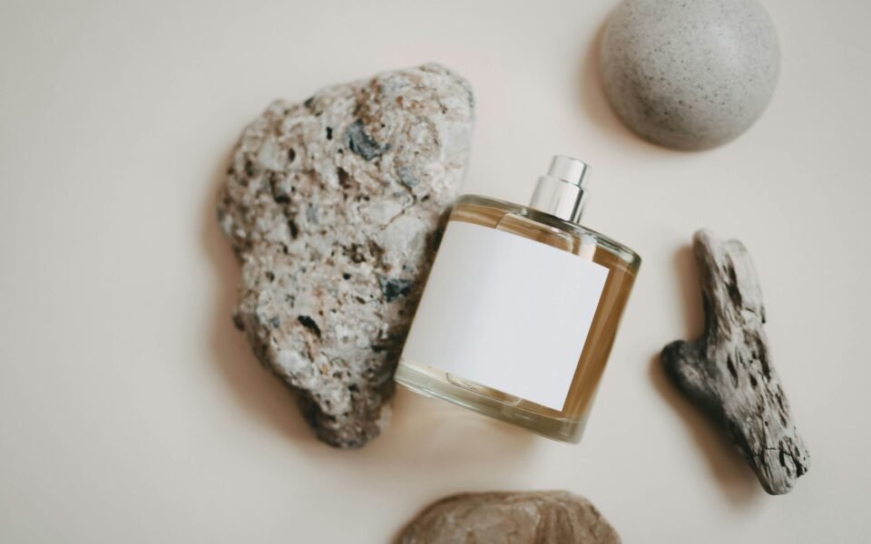Frasco de perfume con la etiqueta en blanco entre piedras sobre fondo claro