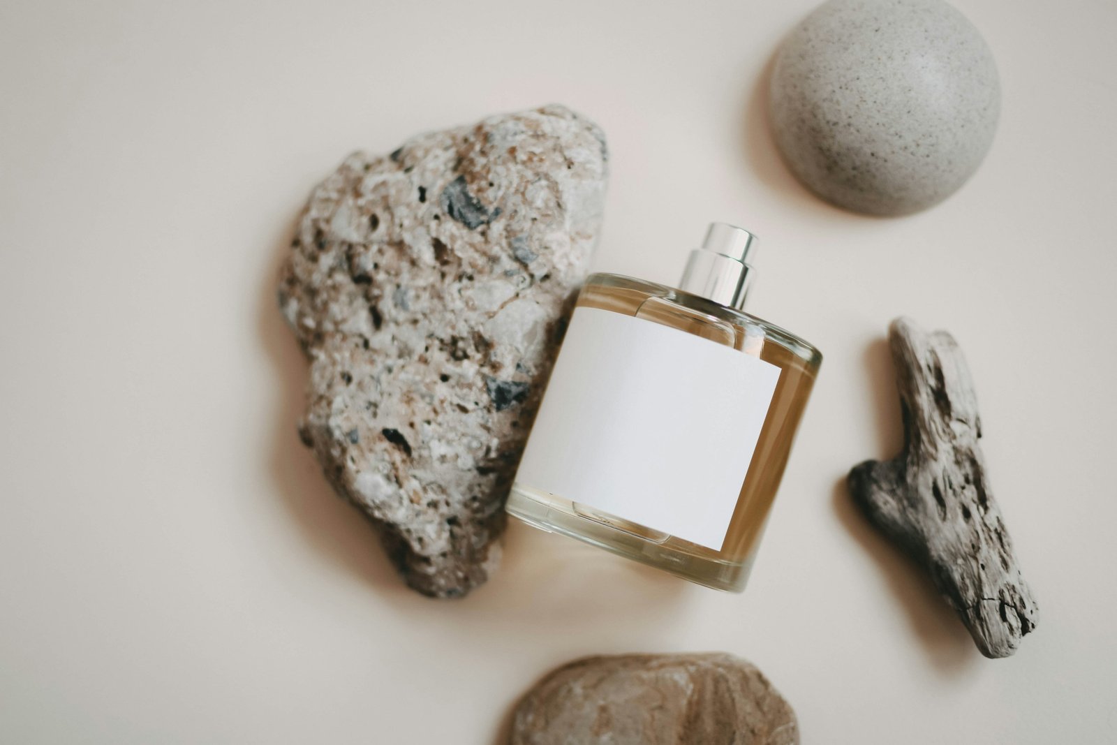 Frasco de perfume con la etiqueta en blanco entre piedras sobre fondo claro