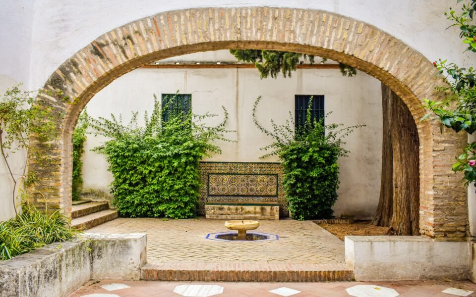 Patio andaluz con arco de ladrillo, banco de azulejos y fuente en Sevilla