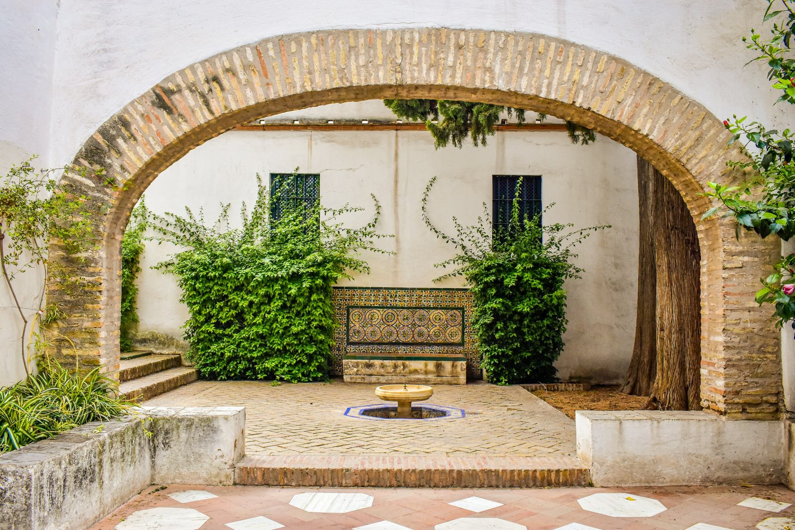 Patio andaluz con arco de ladrillo, banco de azulejos y fuente en Sevilla