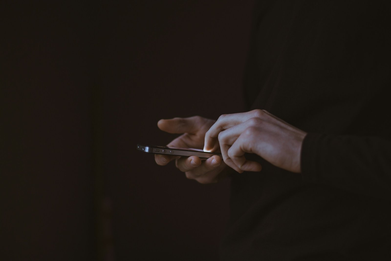 Manos que manejan un teléfono móvil sobre fondo oscuro