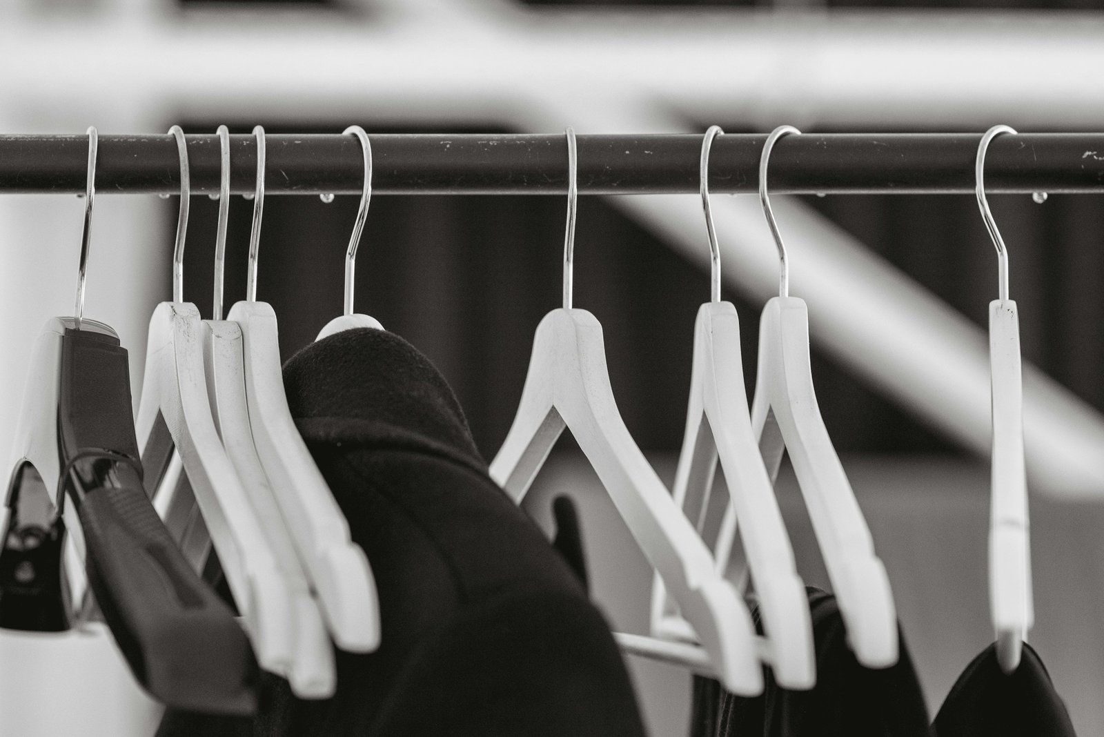 Perchas blancas casi vacías colgadas de una barra en blanco y negro