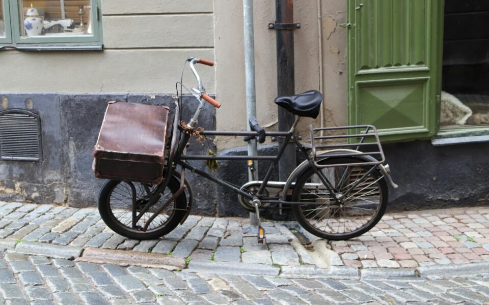Bicicleta de reparto antigua con caja de cuero aparcada en una calle empedrada