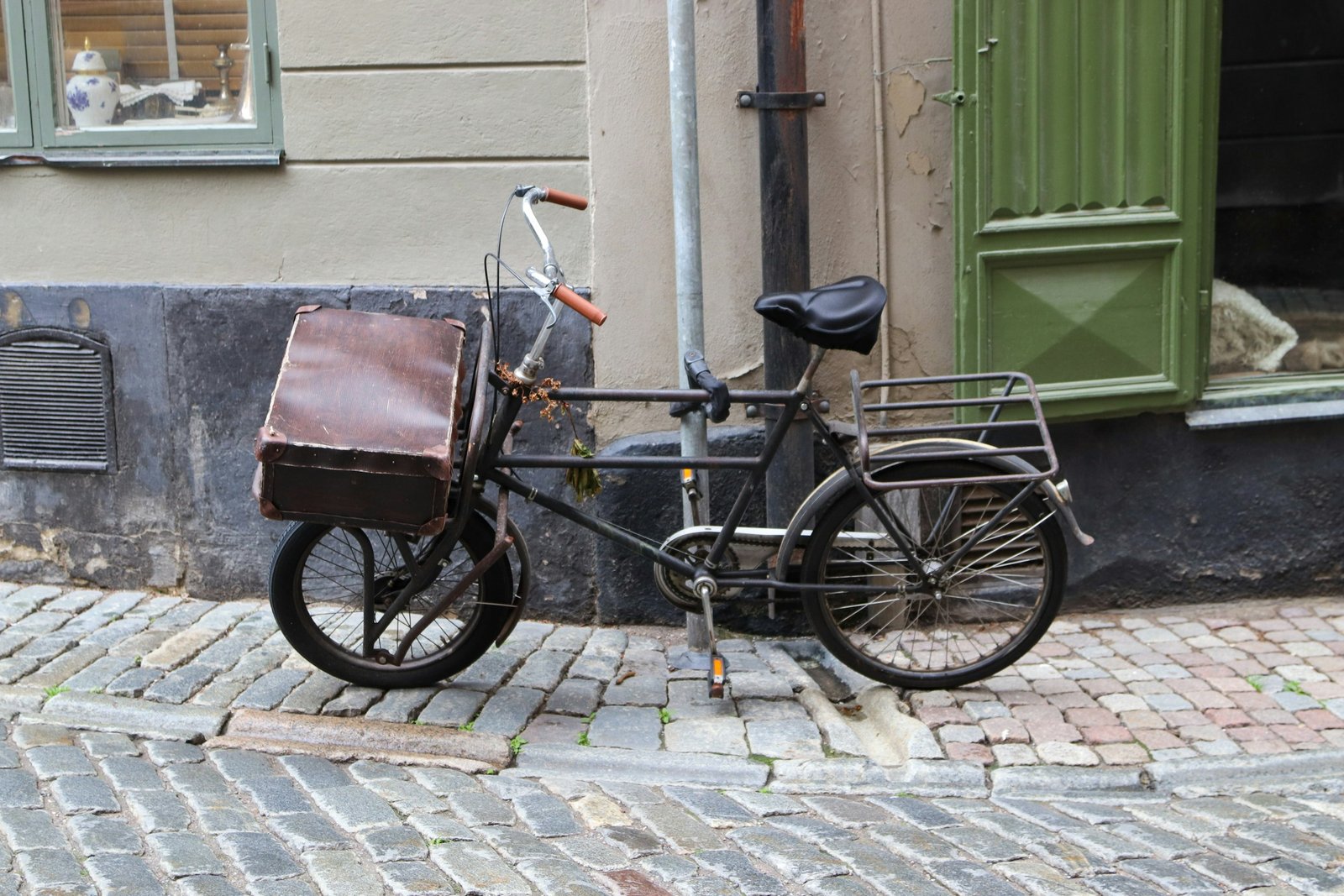 Bicicleta de reparto antigua con caja de cuero aparcada en una calle empedrada