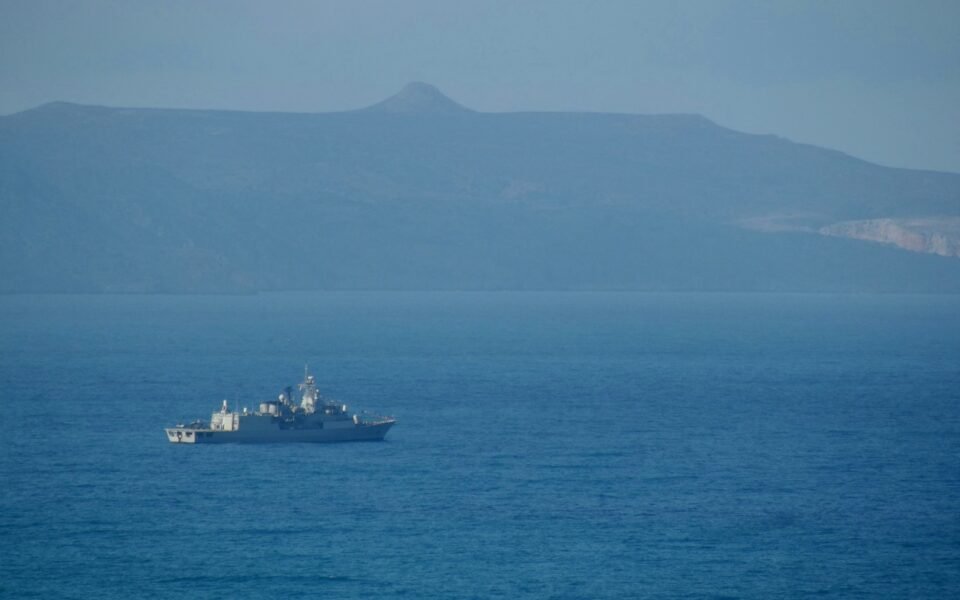 Fragata gris navegando en mar abierto frente a una costa montañosa