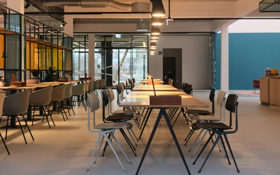 Espacio de coworking vacío con mesas largas, sillas y lámparas colgantes