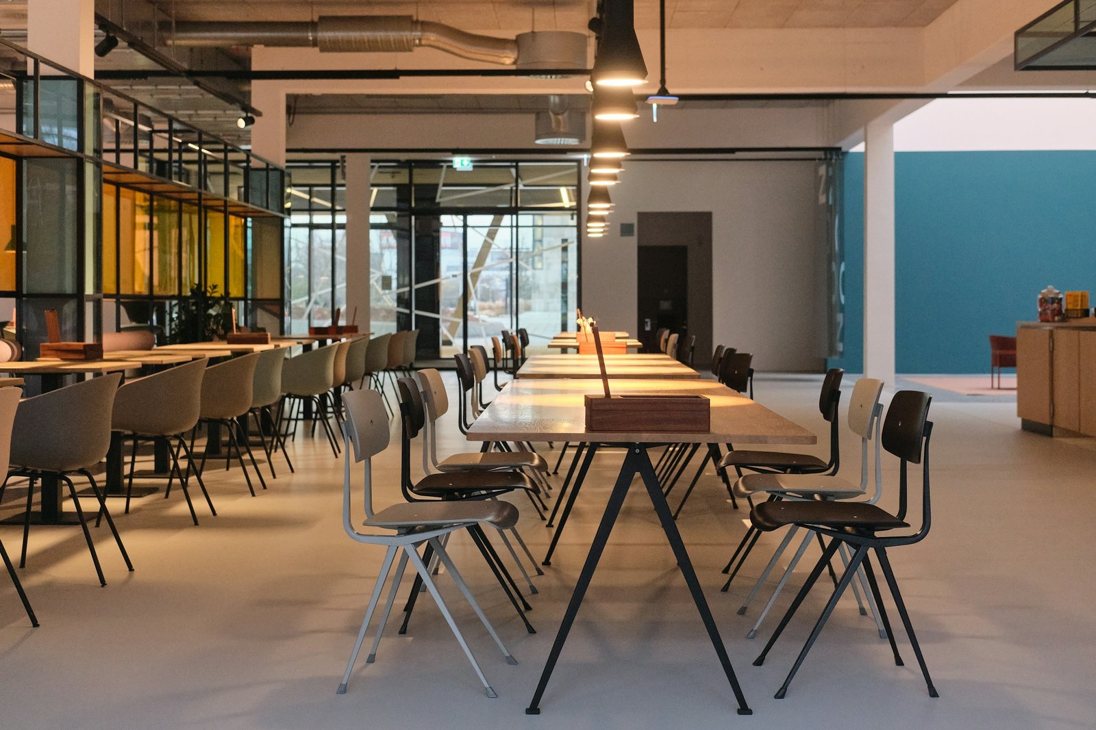 Espacio de coworking vacío con mesas largas, sillas y lámparas colgantes