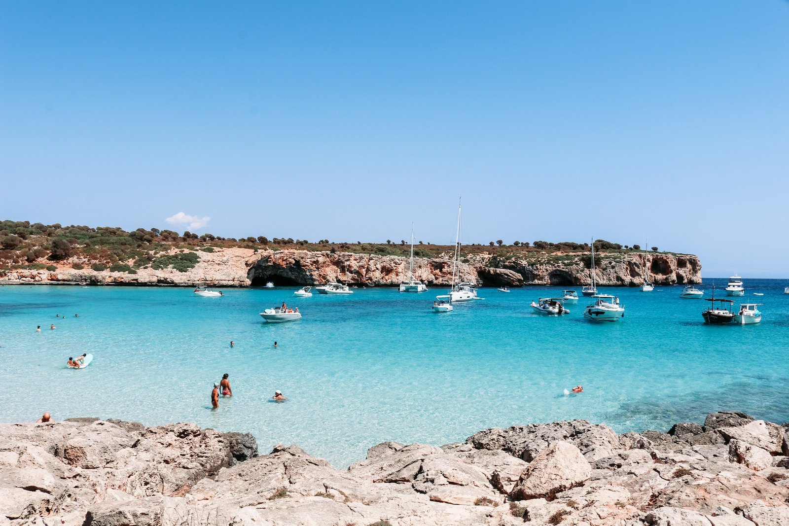Bañistas y barcos fondeados en una cala de aguas turquesa